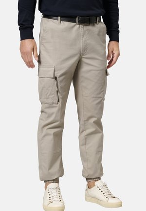 Beige Cargo-Hosen mit elastischen Bündchen, mehreren Seitentaschen und einem robusten Stoff. Getragen mit weißen Turnschuhen und einem dunklen Langarmshirt.