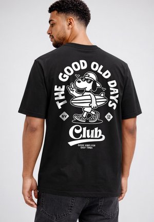 Man wearing black T-shirt with surfing dog cartoon, text "The Good Old Days Club," and "Good Vibes for Easy Times" on the back.