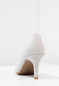 Šedá semišová lodička s vysokým podpatkem, špičatou špičkou, štíhlým podpatkem a hladkým povrchem. Podešev má jemný branding detail.