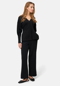 Czarny kardigan na guziki z dekoltem w serek, luźnym krojem i długimi rękawami, zestawiony z czarnymi szerokimi spodniami i czarnymi balerinami.