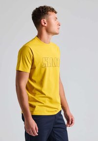 T-shirt en coton jaune à manches courtes avec un imprimé graphique du mot "SLAND" en noir contrasté. Design classique à col rond.