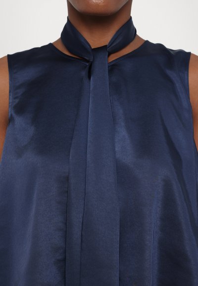 Navy blue sleeveless blouse in satin fabric with a high neck and bow detail, featuring a smooth texture and subtle sheen.