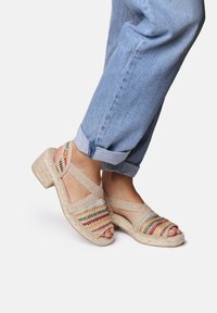 Sandali intrecciati beige con accentuazioni a strisce multicolori e cinturino alla caviglia, dotati di un tacco in wedge testurizzato e design open-toe.