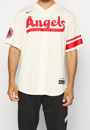 Homme portant un maillot de baseball blanc avec un texte rouge "Angels", des bandes rouges sur les manches et le logo des Los Angeles Angels sur le bras gauche.