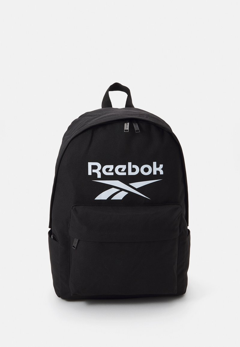 Črn nahrbtnik z gladko teksturo, ki ima velik bel logotip Reebok, dvojno zadrgo in sprednji žep.