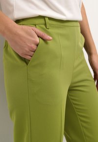 Zelené střihové kalhoty vyrobené z hladké látky, s boční kapsou, přiléhavým střihem a čistým zakončením švů.