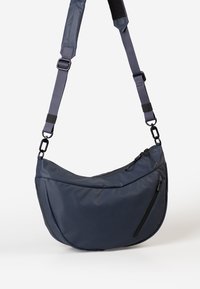 Borsa a spalla blu navy in materiale impermeabile liscio, con due tasche con zip, una forma curva e una tracolla regolabile.