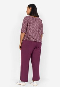 Top viola a fantasia con maniche corte abbinato a pantaloni larghi di un viola uniforme. L'outfit presenta una vestibilità comoda e un tessuto morbido.