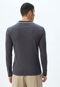 Polo shirt met lange mouwen in donkergrijze ribstof met een contrasterende kraag. Bevat een rechte onderzoom en aansluitende mouwen.
