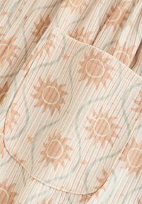 Tissu rayé beige et blanc avec une poche, présentant un motif de formes de soleil marron clair reliées par de fines lignes grises.