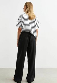 Witte en zwarte gestreepte oversized t-shirt, gecombineerd met losse zwarte broeken. De stof lijkt zacht; de broeken hebben een elastische tailleband.