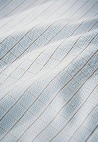 Tessuto azzurro chiaro con un delicato motivo a griglia di sottili linee marroni che creano piccoli quadrati, mostrato con pieghe morbide e dettagli di texture.