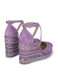 Sandali con zeppa in suede viola con cinturini alla caviglia. Presentano una texture intrecciata e decorazioni sulla zeppa. Suola piatta per stabilità.