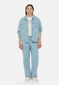 Chaqueta de denim azul claro con grandes bolsillos, combinada con una camiseta azul claro y jeans de pierna ancha a juego. Zapatillas blancas completan el look.