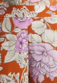 Tissu orange avec de grands motifs floraux violets et blancs et des feuilles détaillées contournées de noir.