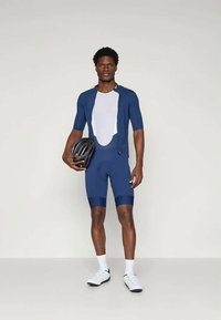 Mornarska biciklistička odjeća s kratkim rukavima i mrežastim umetcima. U kombinaciji s crnom kacigom, bijelim čarapama i biciklističkim cipelama.