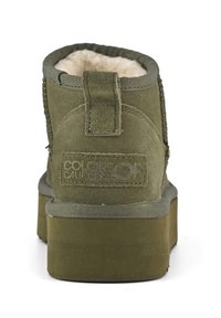 Olive green ankle boot with a textured suede finish, soft cream interior lining, and a flat rubber sole. Features a stitched back tab.