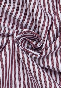 Gestreepte stof met afwisselend bordeauxrode en witte strepen, met een gladde textuur en een opvallend diagonaal patroon, elegant gevouwen.