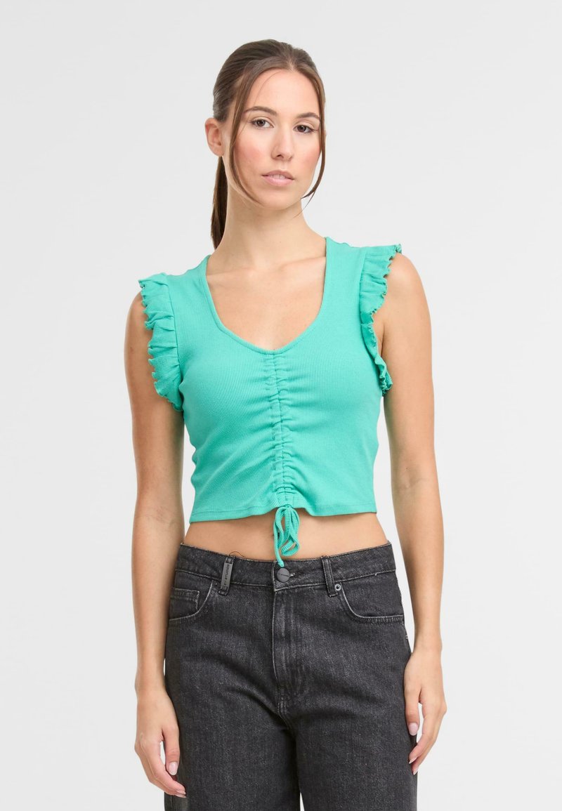 Turkusowy krótki top z falbanami na rękawach, z przodu marszczony i z wiązaniem na dole. Połączony z ciemnoszarymi dżinsami.
