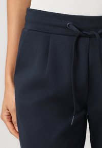 Mörkblå joggingbyxor i strukturerat tyg, med dragsko i midjan, veck och sidofickor för extra bekvämlighet.