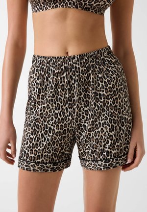 Mujer con pantalones cortos de cintura elástica con estampado de leopardo y top corto a juego, de pie con las manos relajadas a los lados.