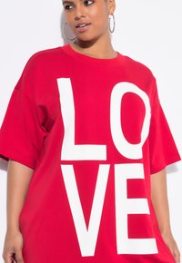 T-shirt oversize rossa in cotone, con grandi lettere bianche in maiuscolo che scrivono "LOVE". Maniche corte e scollo tondo.