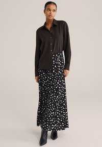 Mustast pikkade varrukatega nööpidega särk, millele on lisatud kõrge vöökohaga must seelik valge täpilise mustriga, millele on lisatud mustad pahkluu saapad.