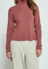 Pull à col roulé cannelé en rose pâle, doté de manches longues et d'une coupe décontractée, associé à un pantalon large crème.