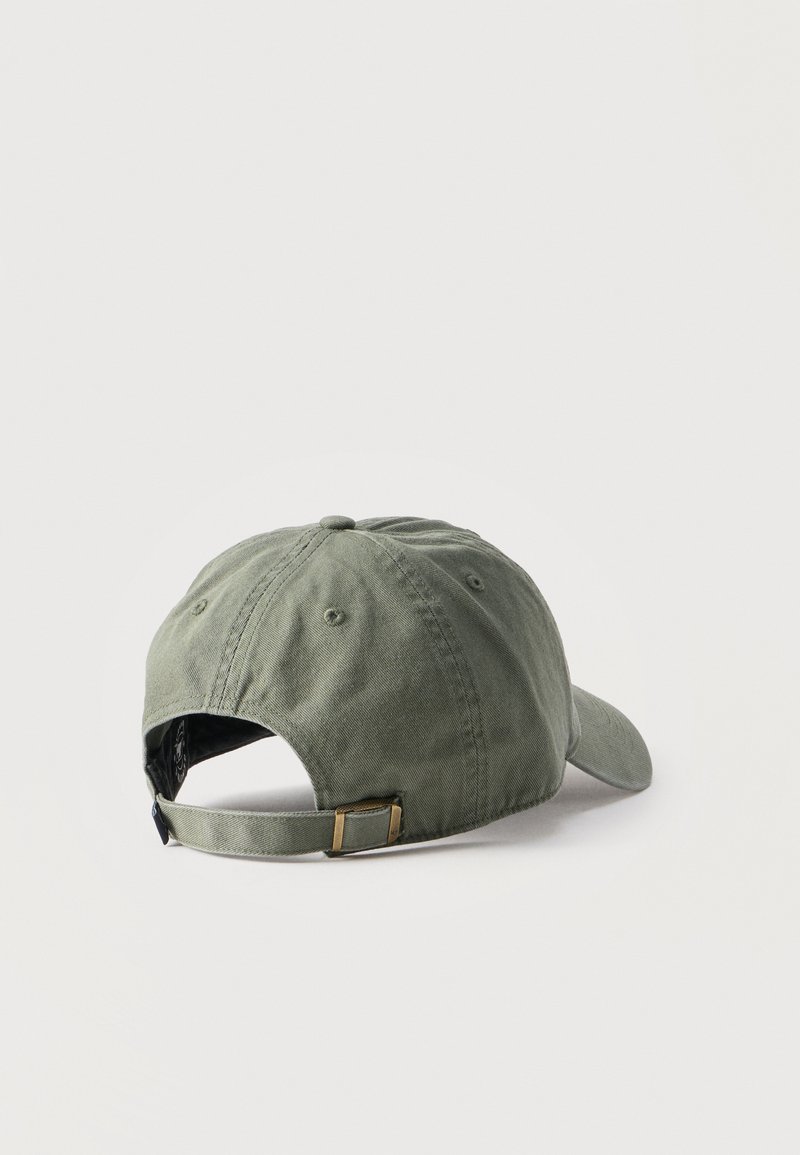 Gorra de béisbol ajustable de color verde oliva vista desde atrás con correa de tela y hebilla de metal sobre un fondo liso.