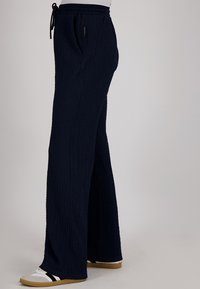 Navyblauwe, gestructureerde wijde broek met een elastische tailleband en trekkoord. Bevat zijzakken en heeft een casual pasvorm. Draag met witte sneakers.