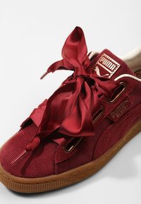 Baskets en velours côtelé rouge avec une semelle épaisse en gomme, présentant des lacets satinés bordeaux surdimensionnés et une étiquette logo Puma dorée sur le côté.