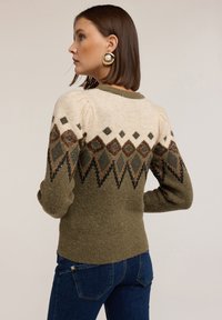 Pulover tricotat cu un schemă de culori crem și măslină, cu modele în formă de diamant în nuanțe de maro închis și negru, mâneci bufante și manșete cu nervuri.