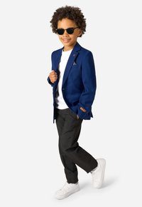 Jūras spēku klasiskā žakete ar zelta akcentiem, balts T-krekls, melnas bikses un baltas kedas. Melni saulesbrilles noslēdz tērpu. Redzami viļņaini mati.