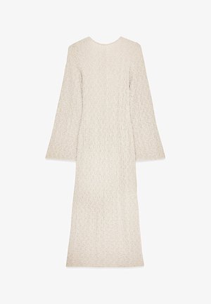 Lång, krämfärgad klänning med texturerad tyg, rund halsringning och utställda ärmar. Enkel, rak silhuett utan synliga knäppningar.