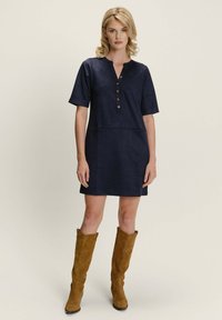 Morski ženski haljina kratkih rukava, s prednjim kopčanjem i opuštenim krojem. Model uparuje haljinu s visokim smeškim suknjičama.