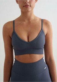 Siva rebrasta bralette z V-izrezom, tankimi naramnicami in kratkim krojem. Tekstura je gladka z diskretnim raztezanjem.