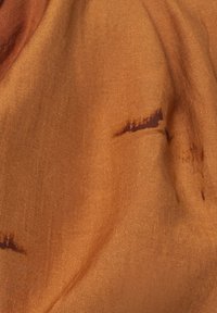 Tessuto in tonalità di arancione caldo con sottili striature più scure, caratterizzato da una texture liscia e una leggera lucentezza, che presenta un design fluido.