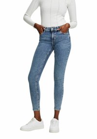 Jeans ajustados de denim azul claro con cintura alta, que cuentan con un clásico diseño de cinco bolsillos y detalles de costura mínimos. Combinados con zapatillas blancas.