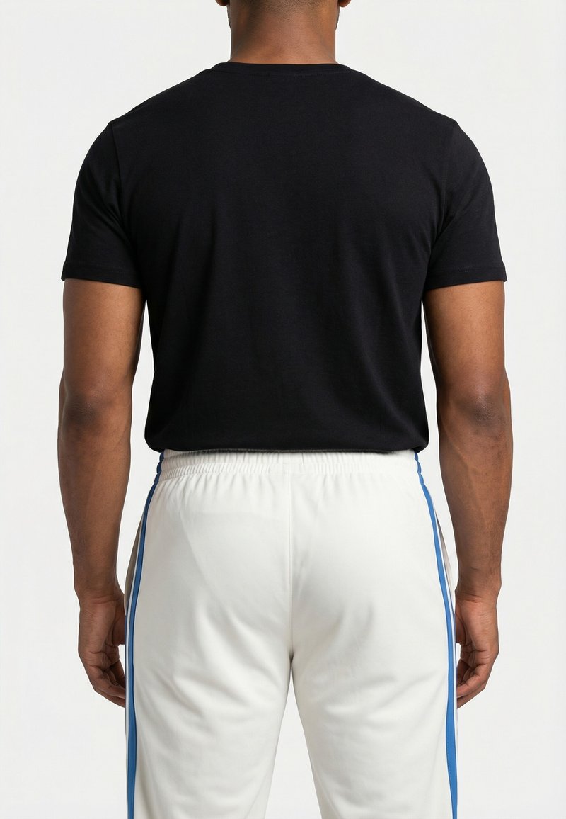 Uomo in piedi di spalle, indossa una maglietta nera a maniche corte e pantaloni bianchi con strisce laterali blu su uno sfondo semplice.