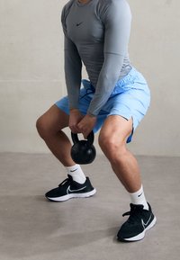 Man i träningskläder som squat:ar medan han håller en svart kettlebell med båda händerna, förbereder sig för träning inomhus.