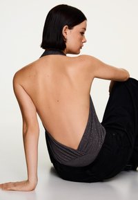 Top gri fără mâneci cu spate adânc decupat, având un design texturat și o strălucire subtilă, asortat cu pantaloni închiși la culoare.