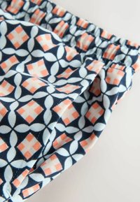 Shorts à taille élastique en tissu léger, présentant un motif géométrique bleu marine, corail et bleu clair, avec une texture lisse.