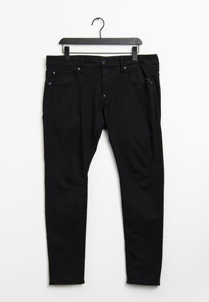 Černé úzké džíny zavěšené na černém ramínku na bílém pozadí, zobrazující přední knoflíky a kapsy.