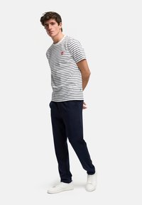 Stripet t-skjorte med korte ermer i hvit og marineblå, med en liten rød logo. Kombinert med marineblå joggebukser og hvite sneakers, med en avslappet passform.
