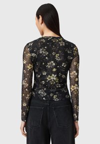 Μπλούζα με μακριά μανίκια από διάφανο μαύρο ύφασμα με floral σχέδιο σε λευκό και κίτρινο, με εφαρμοστή γραμμή και στρογγυλή λαιμόκοψη.