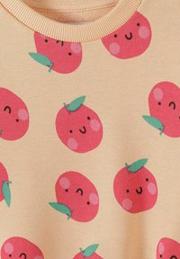 Tissu beige avec motif répété de pommes rouges souriantes aux joues roses et feuilles vertes autour d'un col rond côtelé.