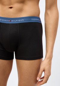 Μαύρα βαμβακερά μπόξερ με μπλε μέση που φέρει το όνομα της μάρκας "TOMMY HILFIGER" σε λευκό, προσφέροντας στενή εφαρμογή και ομαλή υφή.