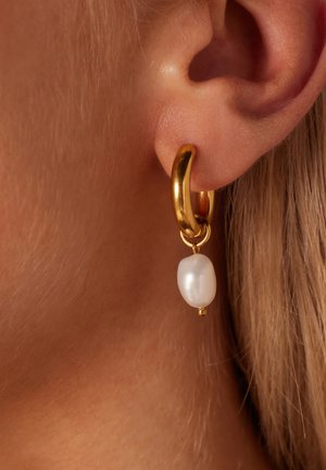 Boucle d'oreille en or avec une goutte de perle blanche en forme d'ovale. La finition en or texturée et le design pendu mettent en valeur la lustre de la perle.