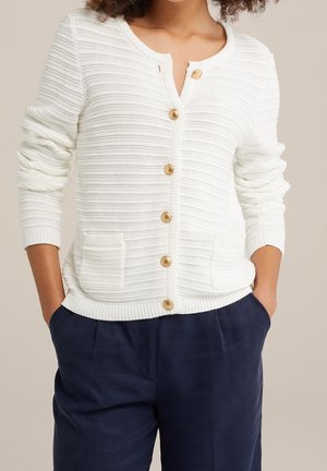 White ribbed cardigan with a round neckline, five golden buttons, and front patch pockets. Fabric has a textured finish.