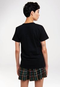 Black cotton T-shirt with short sleeves, round neckline, and a relaxed fit, paired with a green plaid pleated skirt featuring red and yellow accents.